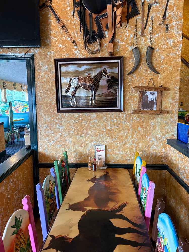 Colorful dining table and hand-painted chairs inside 2 Margaritas Allyn with horse artwork and decorative wall pieces